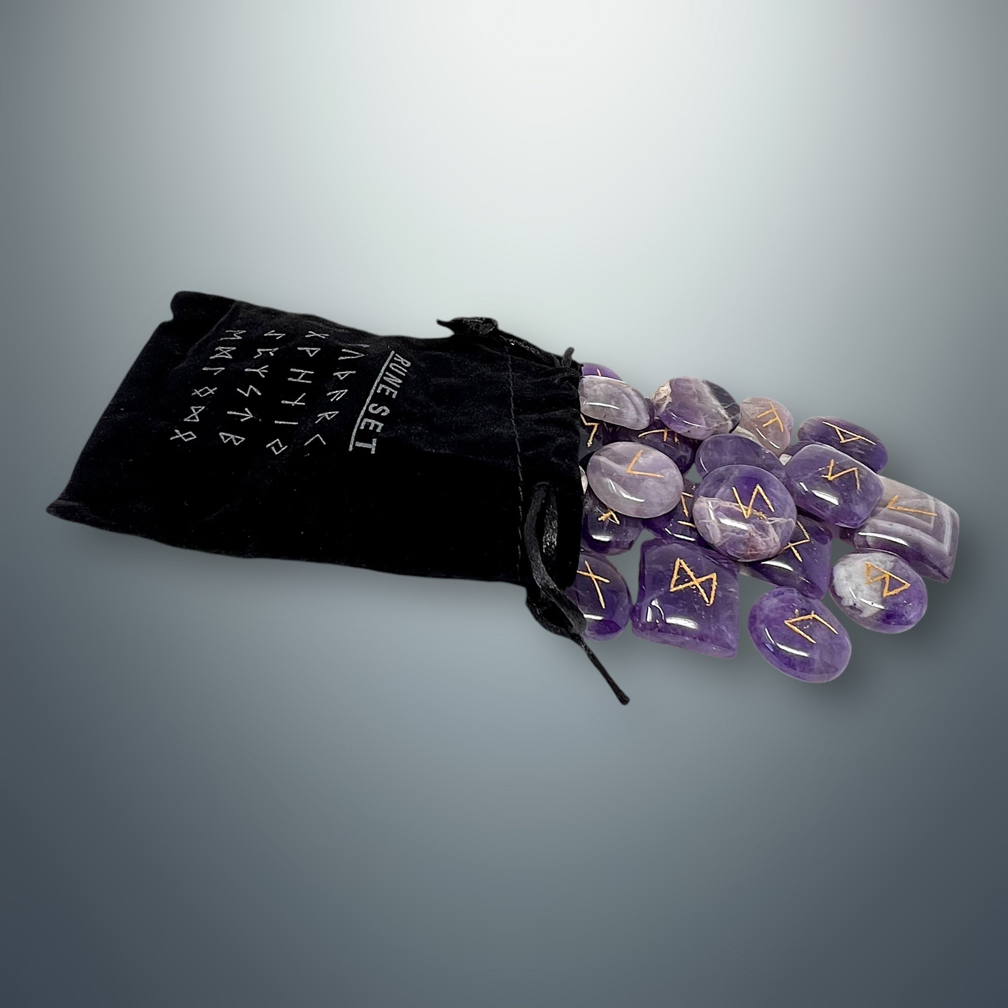 Bolsa pequeña de terciopelo negra con inscripciones rúnicas, de la cual salen algunas runas de amatista morada.