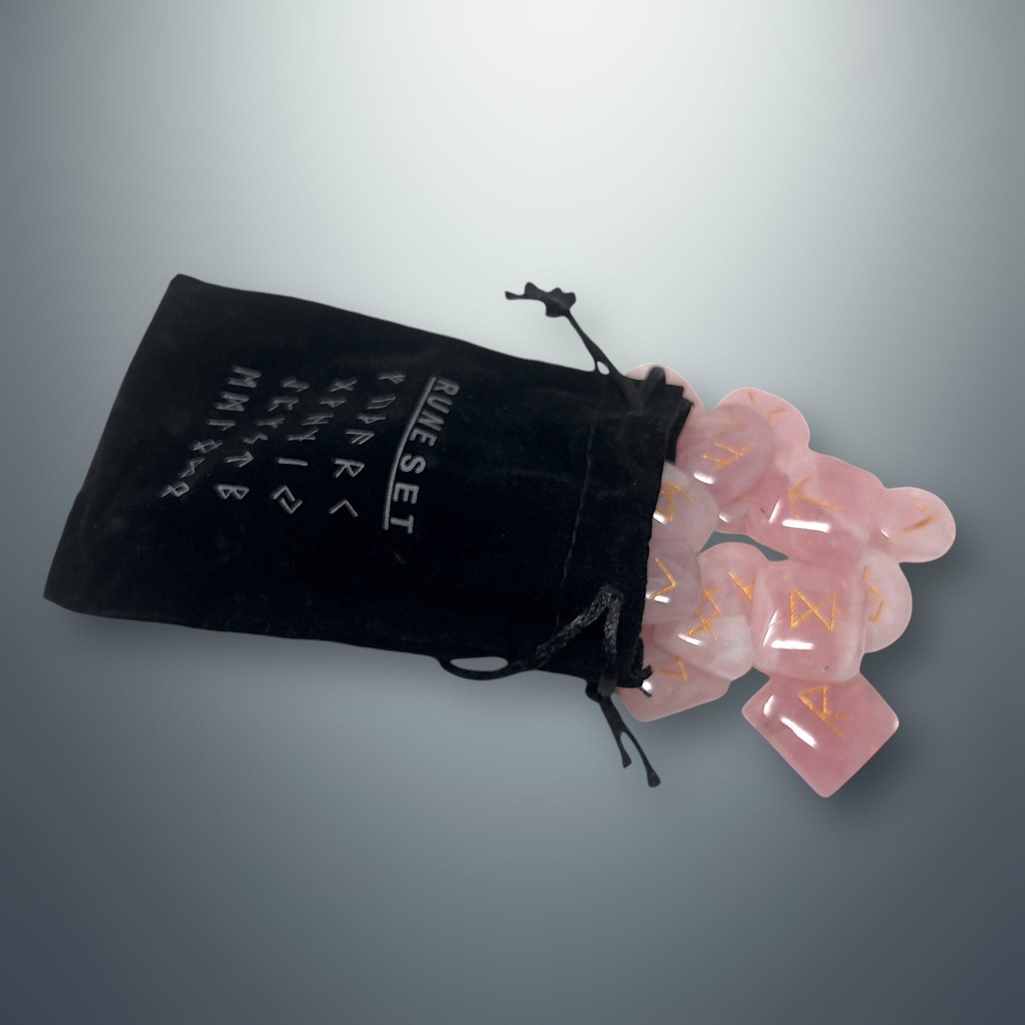 Bolsa pequeña de terciopelo negra con inscripciones rúnicas, de la cual salen algunas runas de cuarzo rosa.