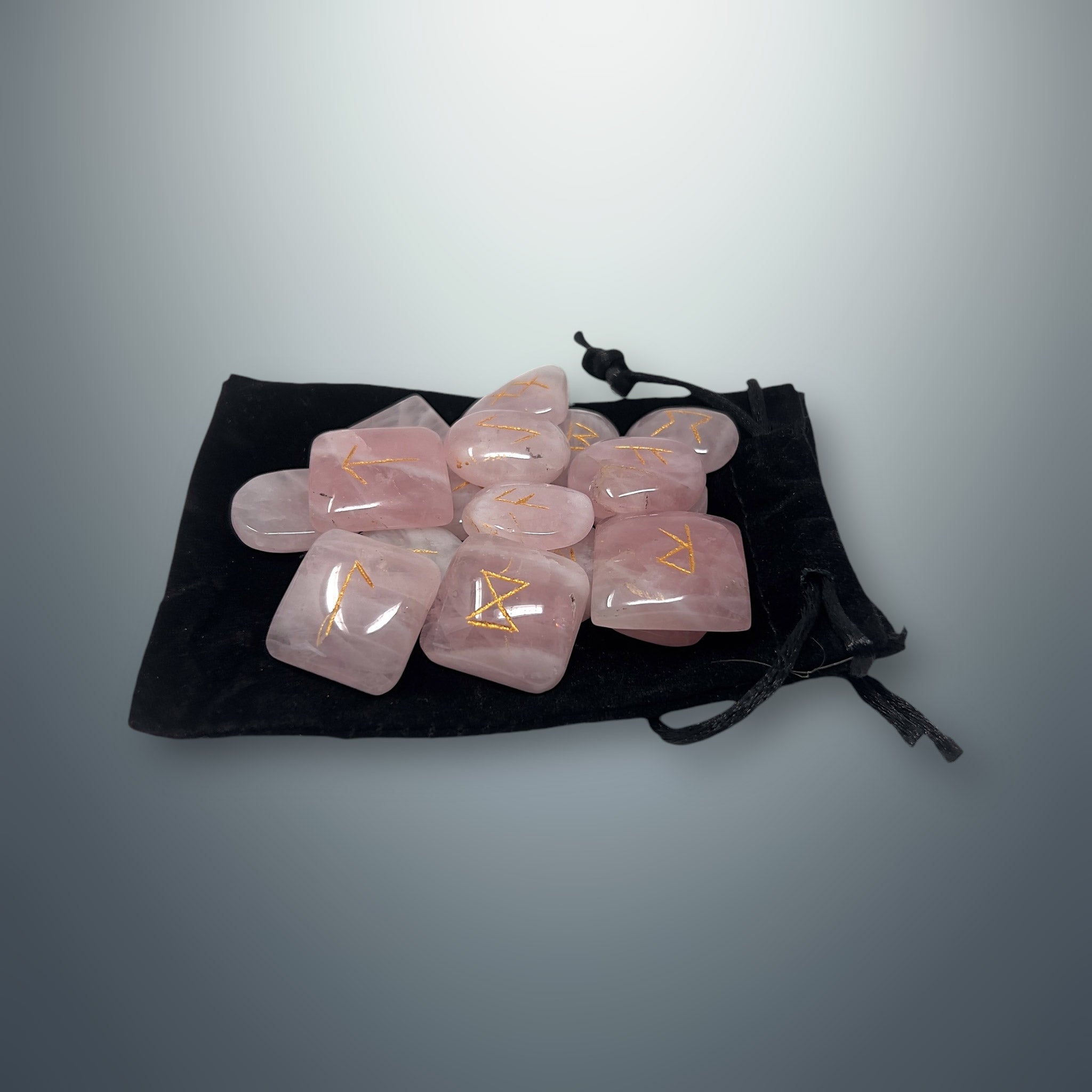 Set de runas de cuarzo rosa sobre una bolsa pequeña de terciopelo negro.
